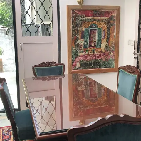Dining nook with a carved wood table under a glass top, teal velvet upholstered chairs, an ornate framed painting, a brass wall sconce