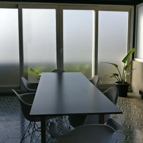 Dining nook with a dark table and mid-century wire-leg chairs on a hexagonal patterned tile floor, backlit by full-height frosted glass doors.