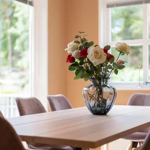 Dining nook with a light wood table, mauve upholstered chairs and a floral centrepiece beside large garden-facing windows