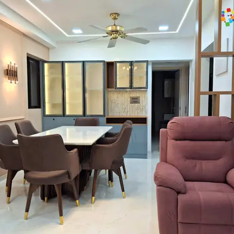 Dining nook with a marble-top table, brass-capped velvet armchairs and a backlit glass crockery unit, opening to a living area with a mauve recliner.