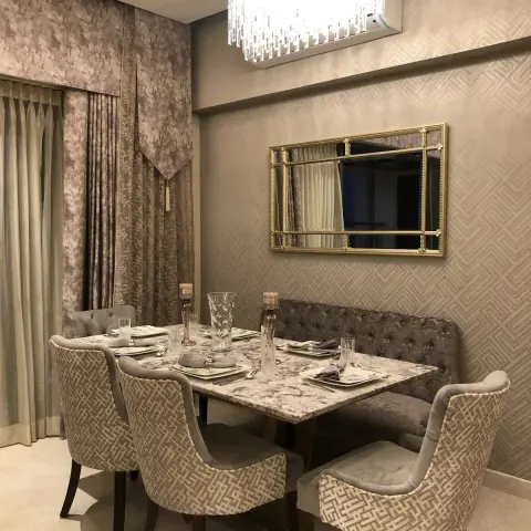 Dining nook with a marble-top table, tufted bench seating against geometric wallpaper, a gold ornate mirror, and a crystal box chandelier.