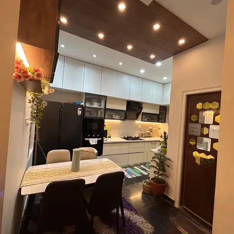Dining nook with a marble-top table for four opening into an L-shaped white gloss kitchen with black appliances and a wood-panelled ceiling drop