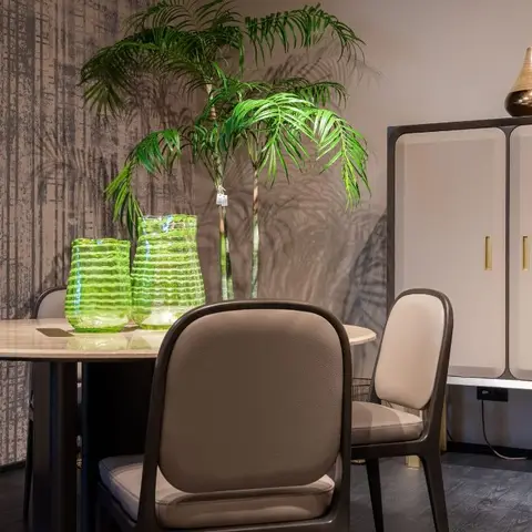 Dining nook with a round marble-top table and taupe leather chairs against textured bronze wallpaper, a tall potted palm