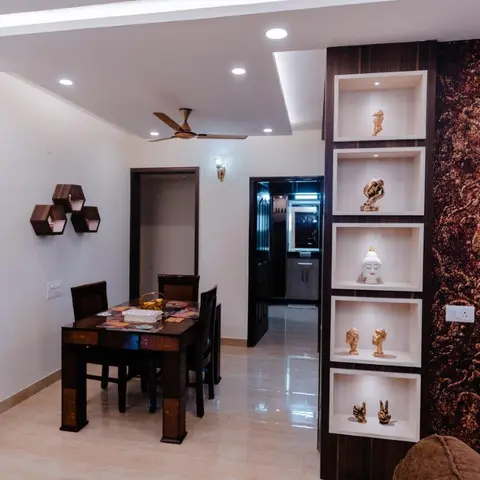 Dining nook with a small inlaid-wood table, a tall wall-mounted display niche styled with statuettes, and a dark textured wallpaper accent wall.