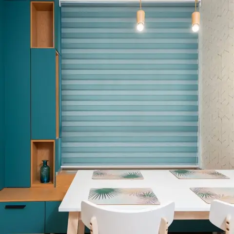 Dining nook with a teal built-in cabinet with open wood-lined niches beside a white table set with tropical-print placemats.