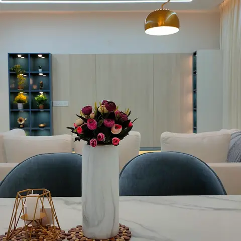 Dining nook with a white marble table, curved blue velvet chairs, and a gold dome pendant light, opening into the living room beyond.