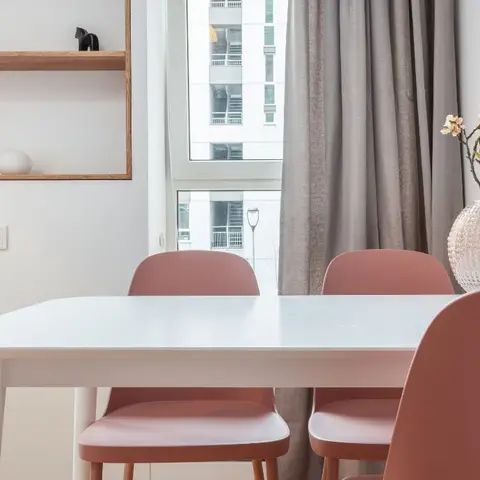 Dining nook with a white oval table, dusty-rose molded chairs and a floating wood display shelf by the window