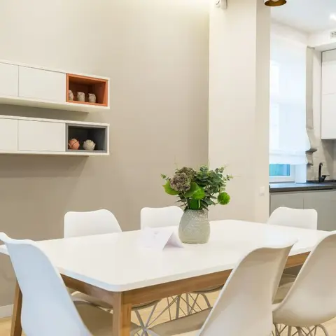 Dining nook with a white-top wood-base table and wishbone chairs beneath floating wall cabinets that frame an orange-lined display niche.