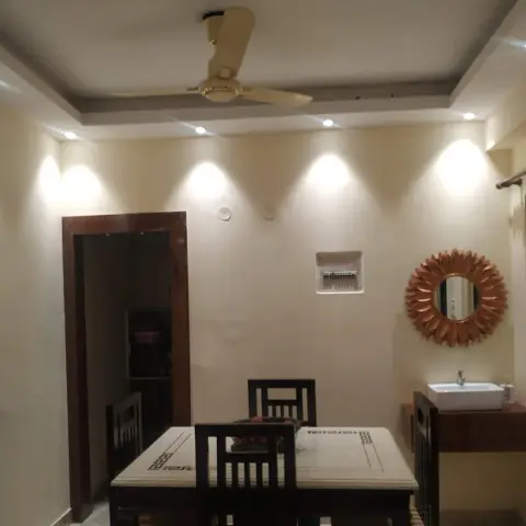 Dining nook with a wooden table and chairs beneath a cove-lit stepped ceiling, a sunburst mirror over a wall-mounted wash basin to the side.