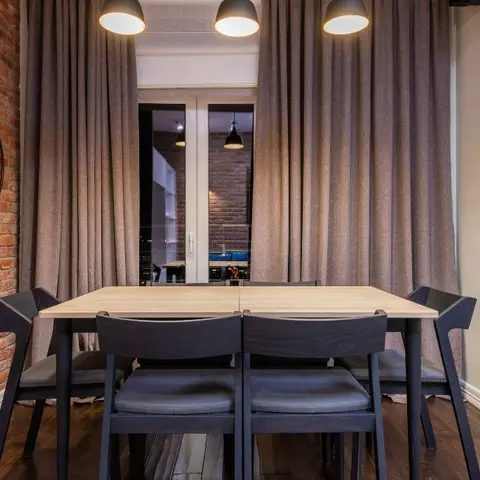 Dining nook with an exposed brick accent wall, a wall-mounted bicycle, and three matching black dome pendants over a light wood table with black chairs.
