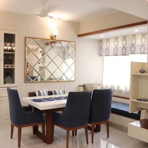Dining nook with navy upholstered chairs and a white table beneath a gold diamond-lattice mirror