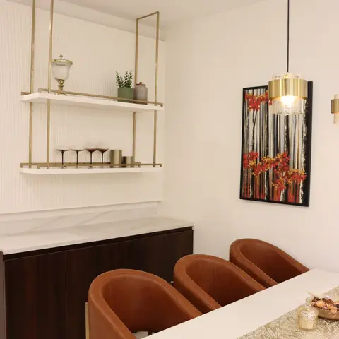 Dining nook with tan leather barrel chairs around a white marble table, a brass-framed open bar shelf styled with glassware
