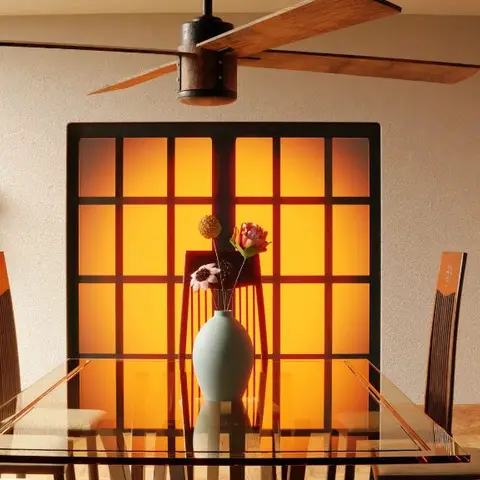 Dining room centred on a glass table with carved dark-wood high-back chairs, facing a backlit amber shoji-grid panel wall.