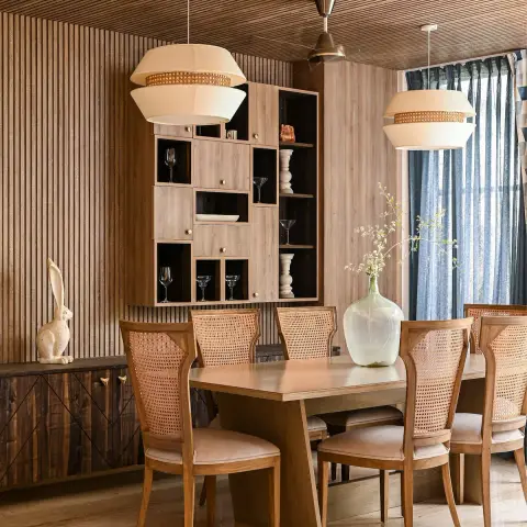 Dining room lined in wood battens across both wall and ceiling, with cane-back chairs around a wedge-leg wooden table