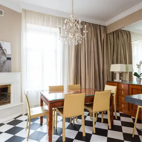 Dining room with a black-and-white checkerboard marble floor, a crystal chandelier, a wood dining table with mustard leather chairs