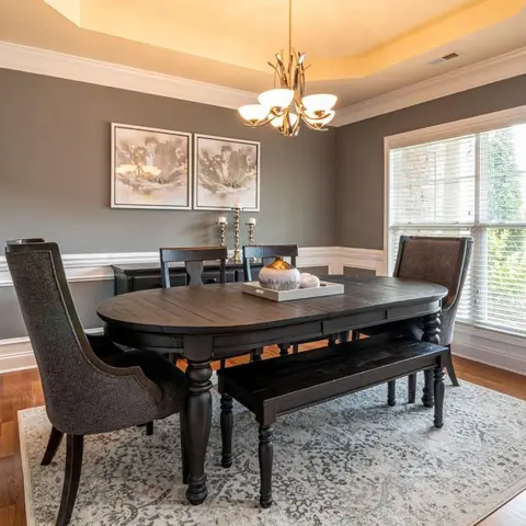 Dining room with a black oval table, matching bench and upholstered chairs on a grey patterned rug, wainscoted grey walls