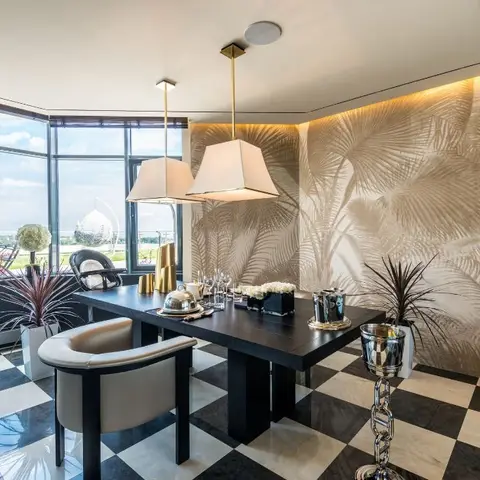 Dining room with a black wood table on a black-and-white checkerboard marble floor, twin fabric pendant lamps, and a metallic palm-frond patterned feature wall.