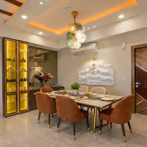 Dining room with a cove-lit ceiling in warm amber light, a bubble-cluster pendant chandelier, a backlit glass crockery display