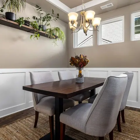 Dining room with a dark wood table and grey upholstered chairs against white board-and-batten wainscoting, under a candle-style chandelier