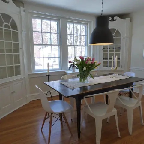 Dining room with a dark wood farmhouse table under a black dome pendant, flanked by built-in arched glass-front display cabinets.