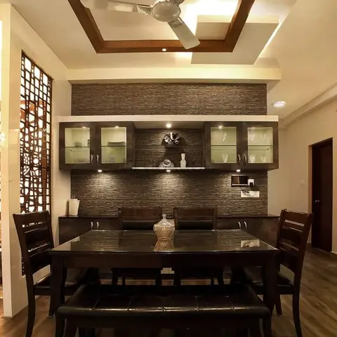 Dining room with a dark wood table and bench set beneath a coffered wood-trim ceiling, a lit glass-front crockery unit on a textured stone wall