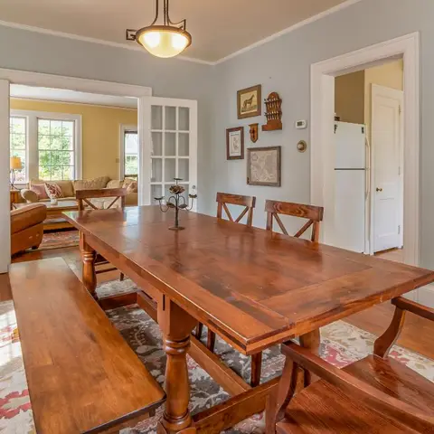 Dining room with a farmhouse trestle table and benches, French glazed doors to the living room, and a curated gallery wall of small framed art.