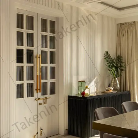 Dining room with a fluted glass-panel double door with gold handles, ribbed wall panelling, a black fluted sideboard styled with glass objects