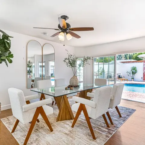 Dining room with a glass-top wood dining table, boucle-upholstered armchairs, arched mirrors, and a fiddle-leaf fig