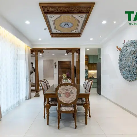 Dining room with a hand-carved wood ceiling medallion above a glass-top wood dining table, ornate carved entrance pillars, sheer curtains