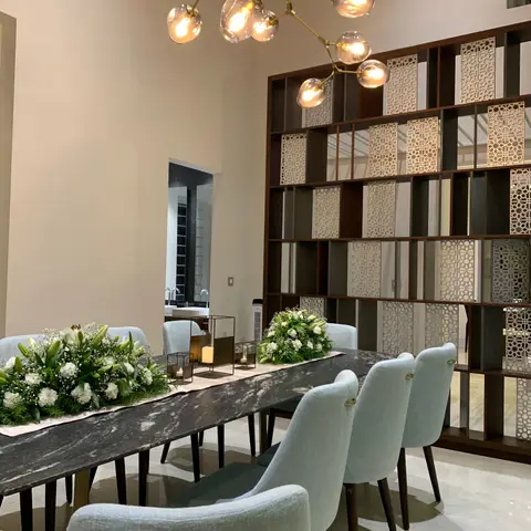 Dining room with a long black marble table set with white floral arrangements under a sculptural branching brass globe chandelier