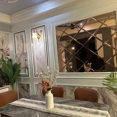 Dining room with a marble table and tan leather chairs against a panelled wall featuring palm-leaf wallpaper insets and a diamond-cut mirror.