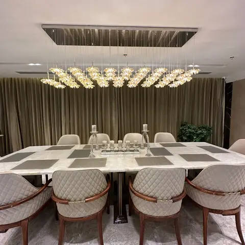 Dining room with a marble table seating eight in quilted leather chairs, beneath an oversized gold floral-cluster chandelier.