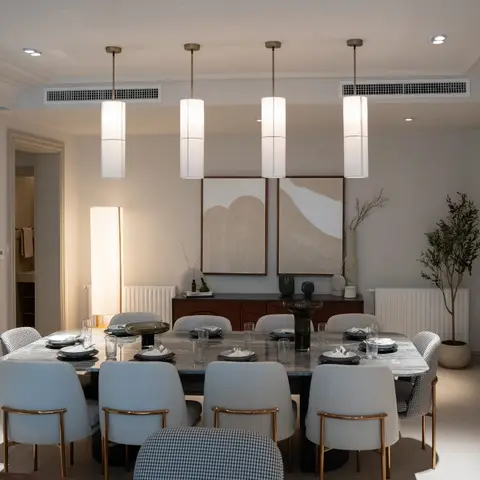 Dining room with a marble table, four cylindrical pendant lights in a row and a pair of abstract artworks above a console.