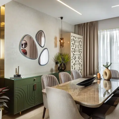 Dining room with a marble table and channel-tufted velvet chairs facing an olive-green carved sideboard beneath a trio of organic-shaped mirrors and brass
