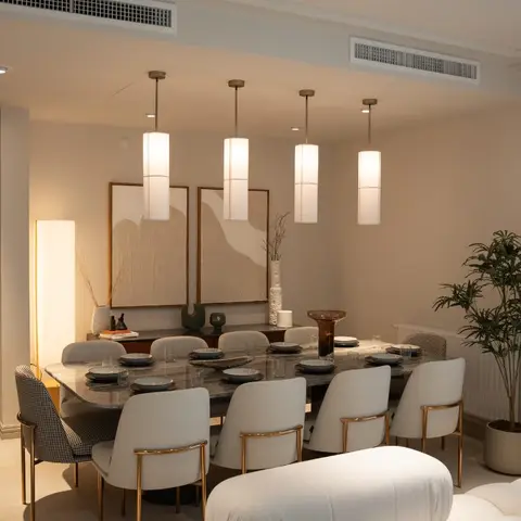 Dining room with a marble-top table, four cylindrical pendant lights at staggered heights and gold-trimmed upholstered chairs, styled console behind.