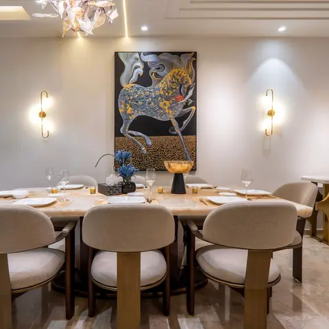 Dining room with a marble-top table set for eight beneath a crystal chandelier, cream upholstered chairs, brass wall sconces flanking a large horse artwork