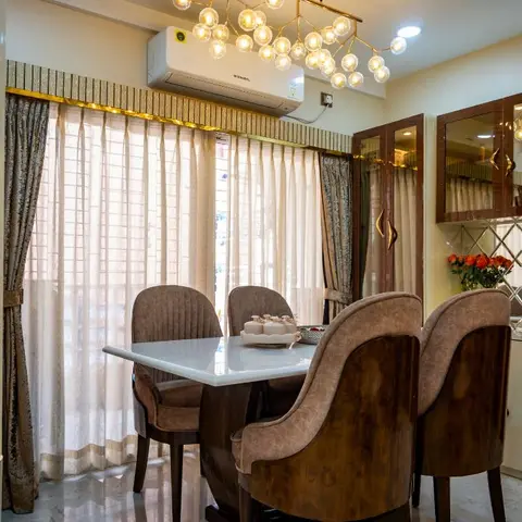 Dining room with a marble-top table and channel-tufted upholstered chairs beneath a gold bubble chandelier