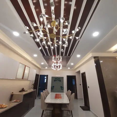 Dining room with a marble-top table under a branching crystal chandelier, set beneath a dark-wood-and-white striped false ceiling.