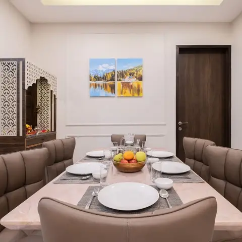 Dining room with a marble-top table set for six in taupe leather chairs, a jaali-fronted pooja console in the corner