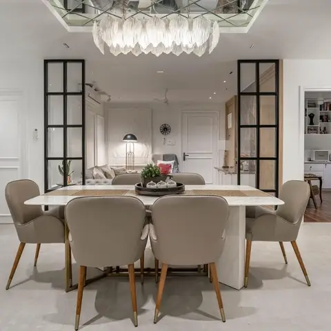 Dining room with a marble-top table surrounded by taupe upholstered chairs on brass legs, under a cascading crystal-leaf chandelier