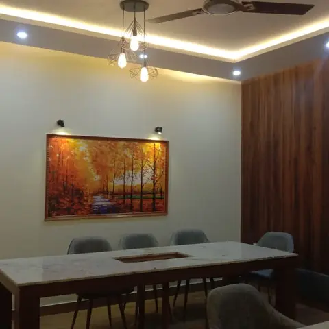 Dining room with a marble-top table beneath a geometric wire-cage pendant cluster, a framed landscape painting lit by picture lights