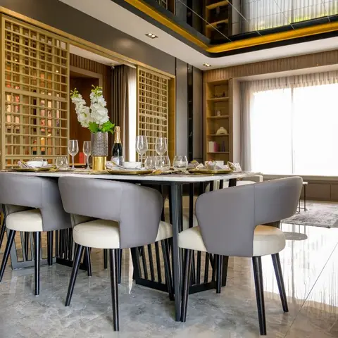 Dining room with a marble-top table and grey leather chairs set for a formal dinner, a gold jaali lattice partition wall