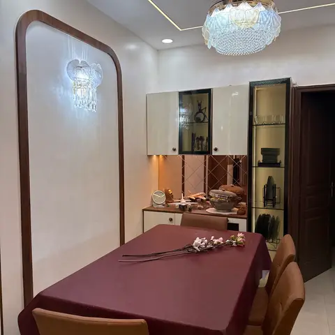 Dining room with a rectangular table under maroon linen, tan leather chairs, a crystal ceiling chandelier matched by a wall sconce set in an arched wood-framed