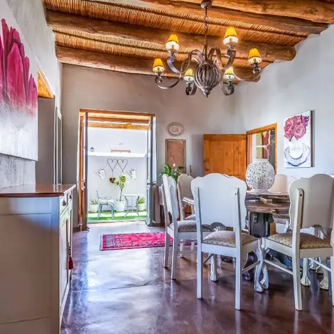 Dining room with a reed-and-timber beamed ceiling, a wrought-iron candle chandelier, white carved dining chairs, and pink floral wall art