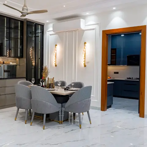 Dining room with a round marble table surrounded by six channel-tufted grey velvet chairs with brass-tipped legs, fluted wall panelling