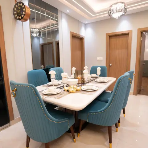 Dining room with a six-seat marble-top table, teal velvet chairs with brass nailhead trim, a crystal chandelier, and a full-height mirrored wall panel.
