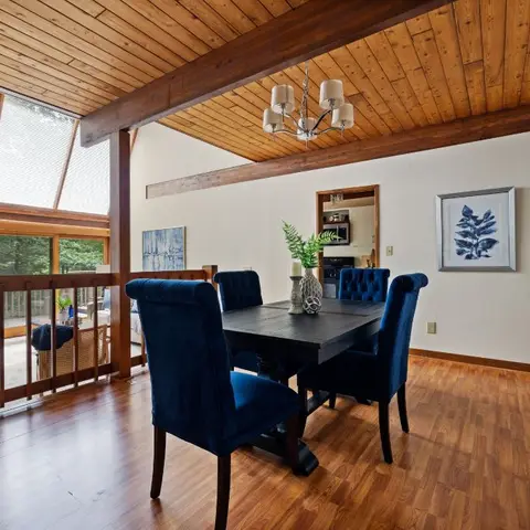 Dining room with a vaulted wood-plank ceiling, a black pedestal table with navy tufted chairs, and a pair of sunburst mirrors on the wall.