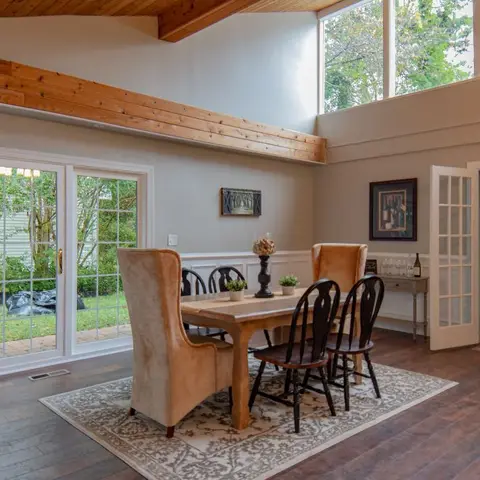 Dining room with a vaulted wood-beam ceiling, wide-plank wood flooring, a farmhouse table with mismatched wingback and spindle chairs