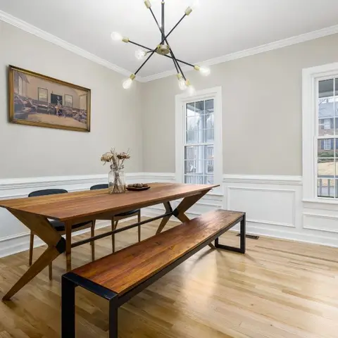 Dining room with a wainscoted cream wall, an X-leg wood table paired with a matching bench, and a sputnik-style chandelier below crown moulding