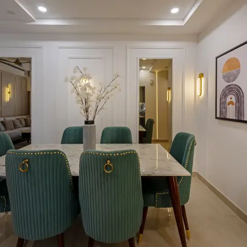 Dining room with a white marble-top table, green channel-tufted velvet chairs with brass nailhead trim and ring pulls, wall panel moulding